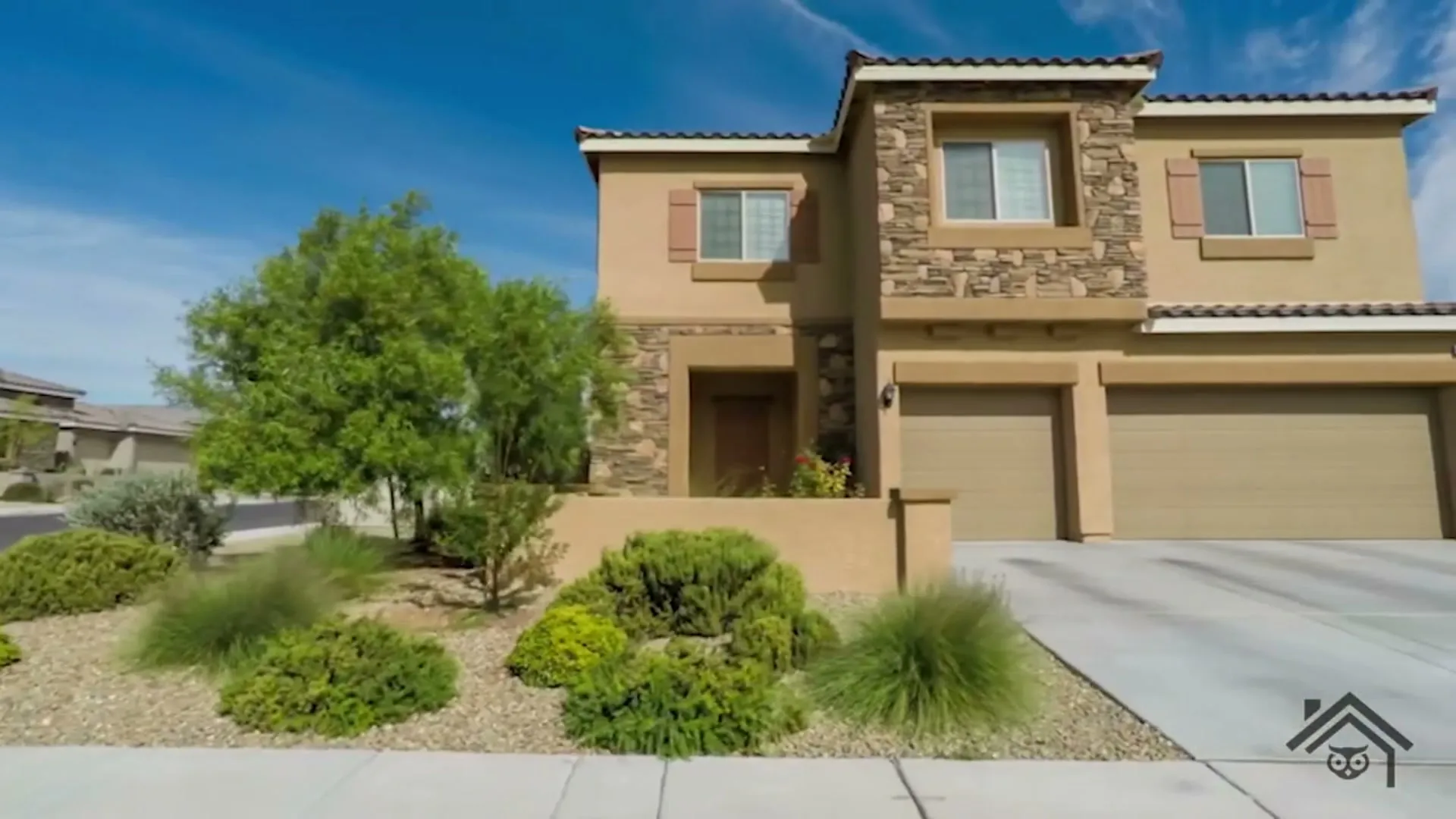Two-story stucco and stone house with a tile roof, three-car garage and a drought-tolerant front yard